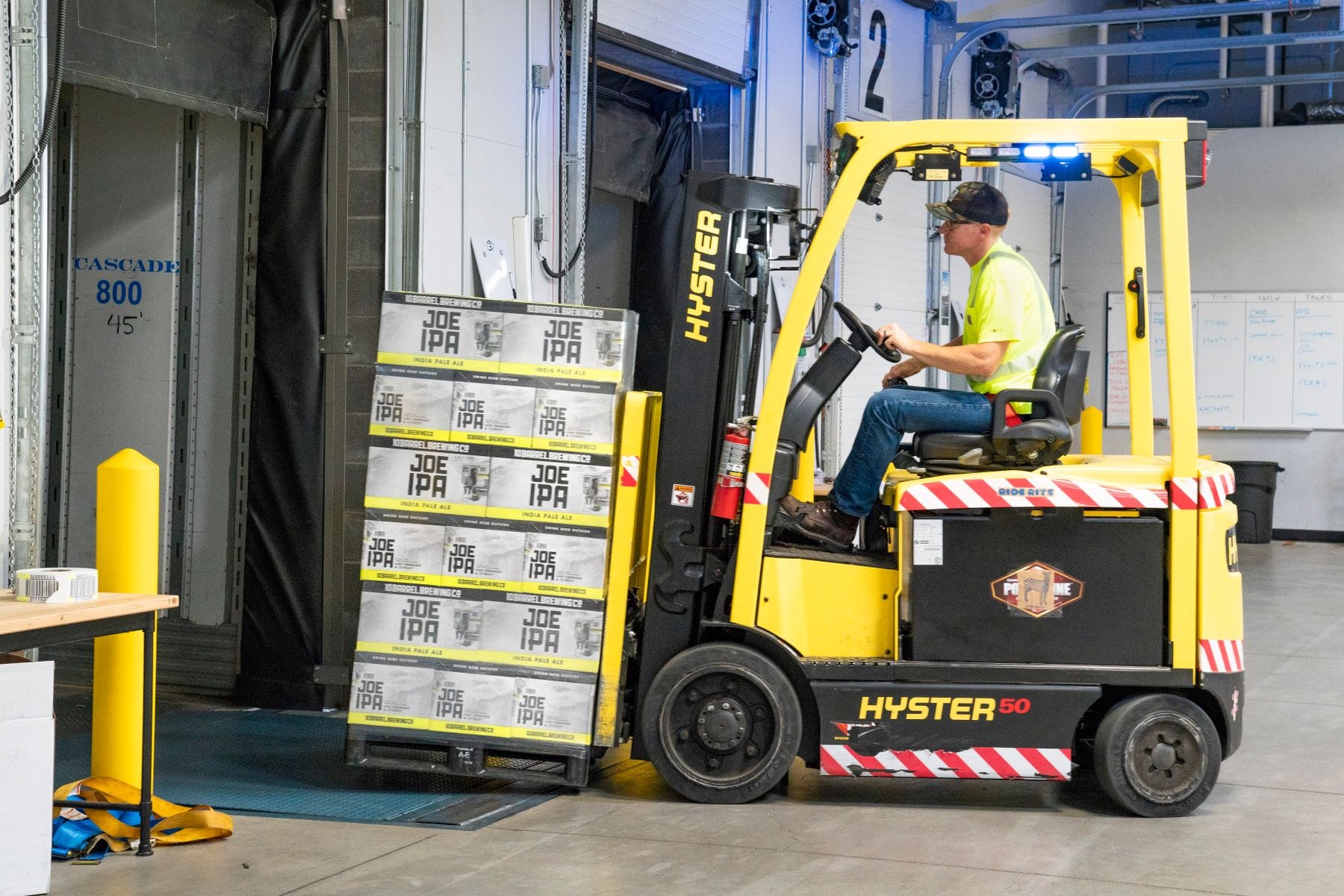 Forklift operator handling a pallet of boxed goods beside a loading dock